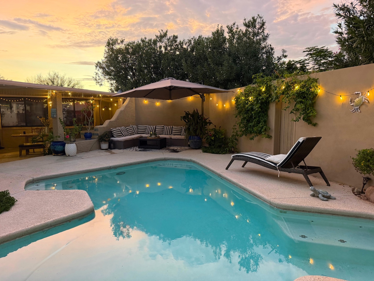 The property’s shared pool at sunset, with lounge seating, an umbrella, and patio lighting